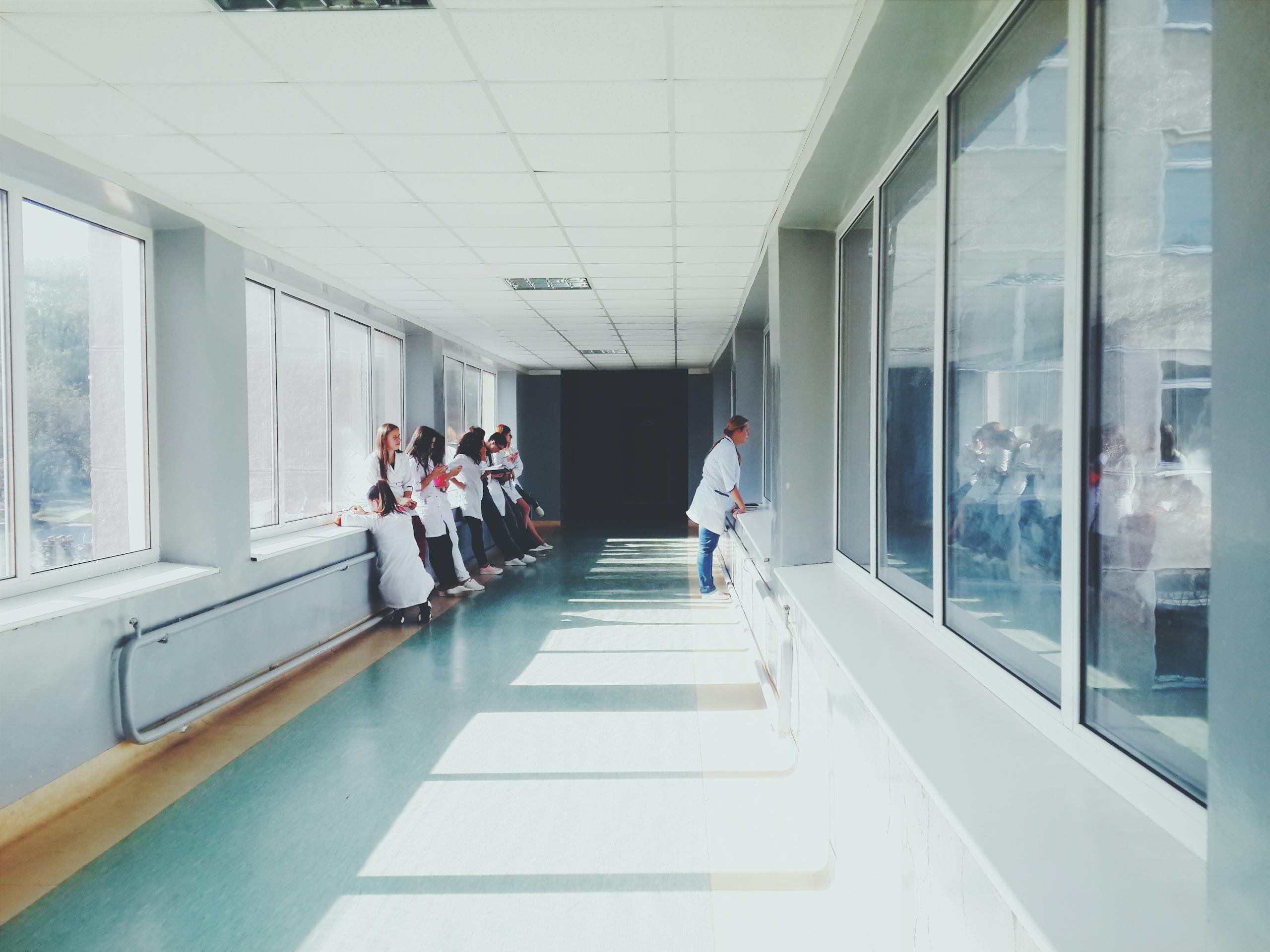 A brightly lit hospital hallway with medical staff in white coats, conveying a professional healthcare environment.